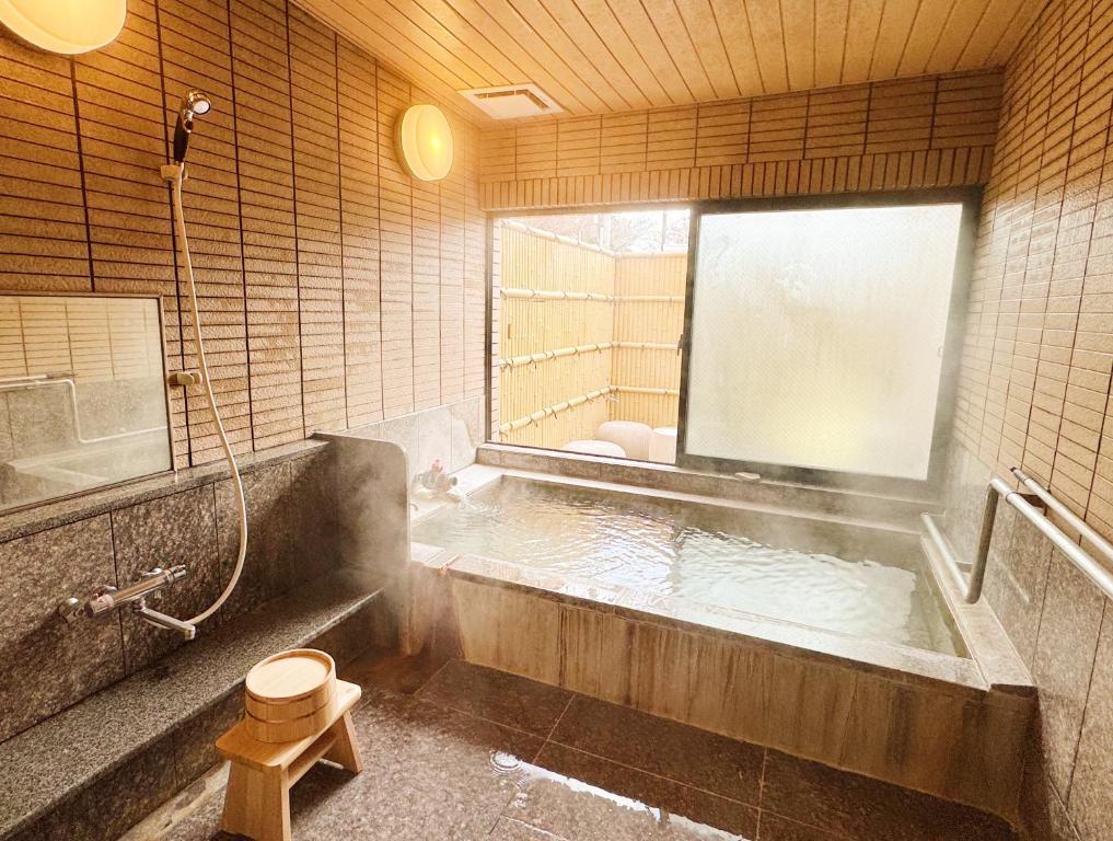 a bathroom with a bath tub with a window at Yunokawa Onsen KOMOREBISO in Hakodate