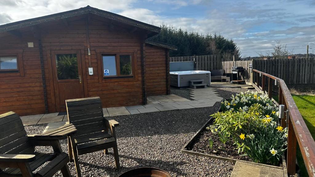 a small cabin with a table and chairs in a garden at Lochinvar - Highland Log Cabin with Private Hot Tub in Airdrie