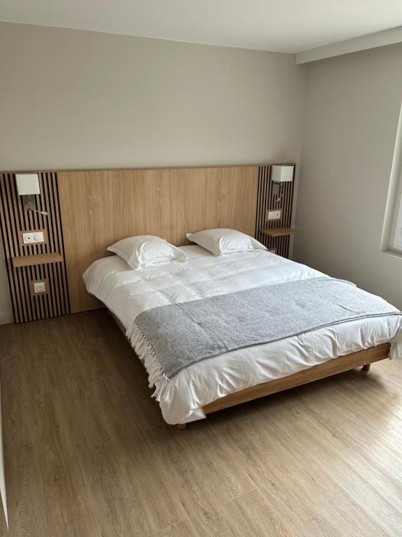 a bedroom with a large bed with a wooden headboard at Hôtel L'escale des Hayons in Esclavelles