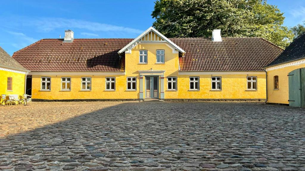 a yellow house with a cobblestone street in front of it at Historic Farmhouse From 1848 in Hårby