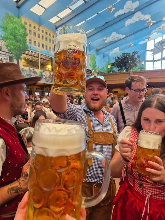 a man holding up two large glasses of beer at Beer Base-Camp 'BASIC PACKAGE' Oktoberfest Camping, with free welcome beer and traditional lederhosen-dirndl shop in Munich