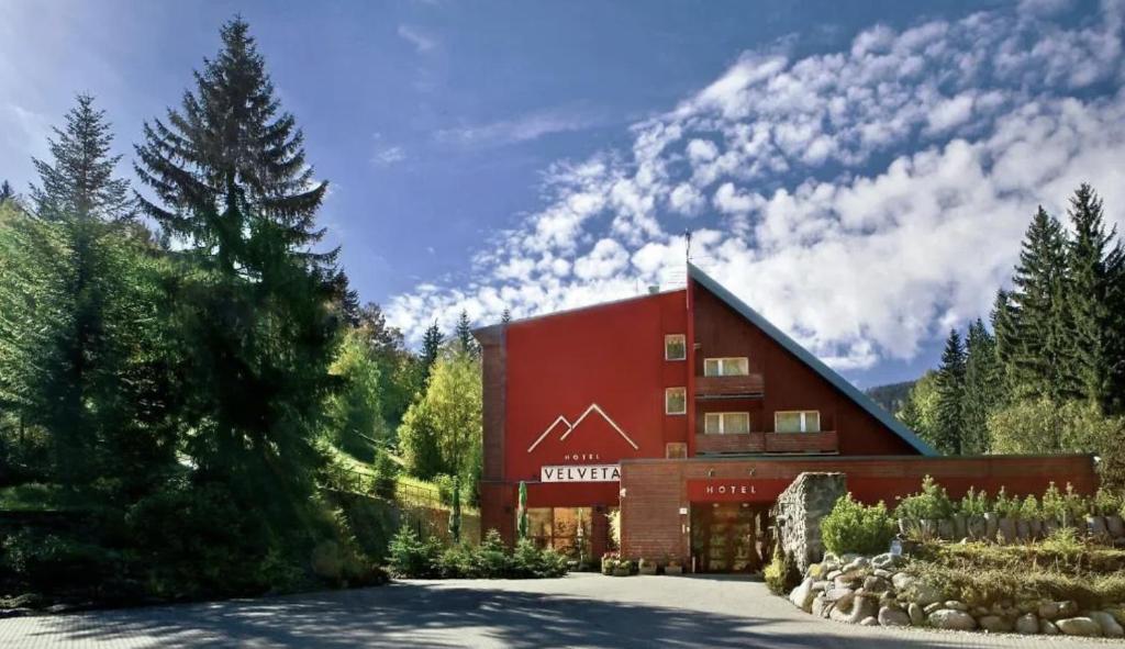 a large red building in the middle of a forest at Hotel Velveta in Špindlerův Mlýn