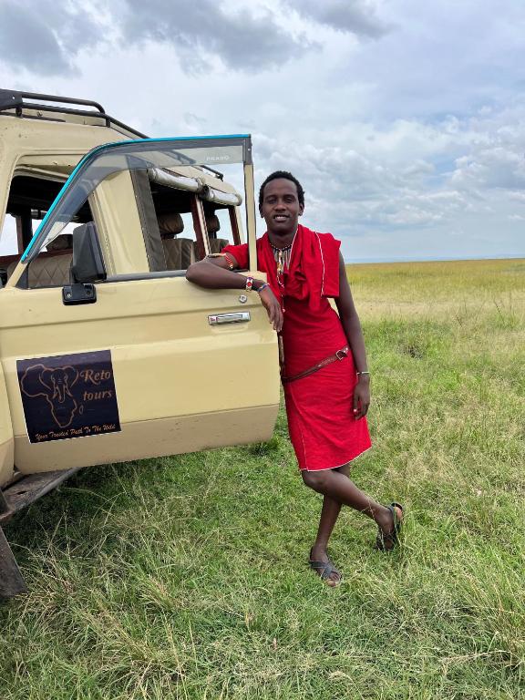 a woman in a red dress standing next to a vehicle at leyianmaasaisafaris in Narok
