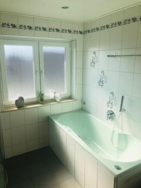 a white bathroom with a tub and two windows at Pension Platzhirsch Vogelsberg in Mücke