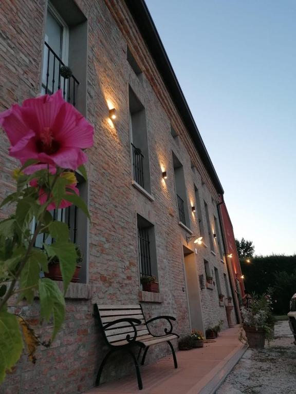a bench next to a brick building with a pink flower at CORTE STELLATA Il Grano Lodging in Bondeno