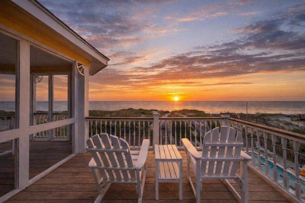 two chairs and a table on a porch with a sunset at Savannah - Nags Head MP 16, Oceanfront, Direct Beach Access, Pool, Hot Tub, Pool Table in Nags Head