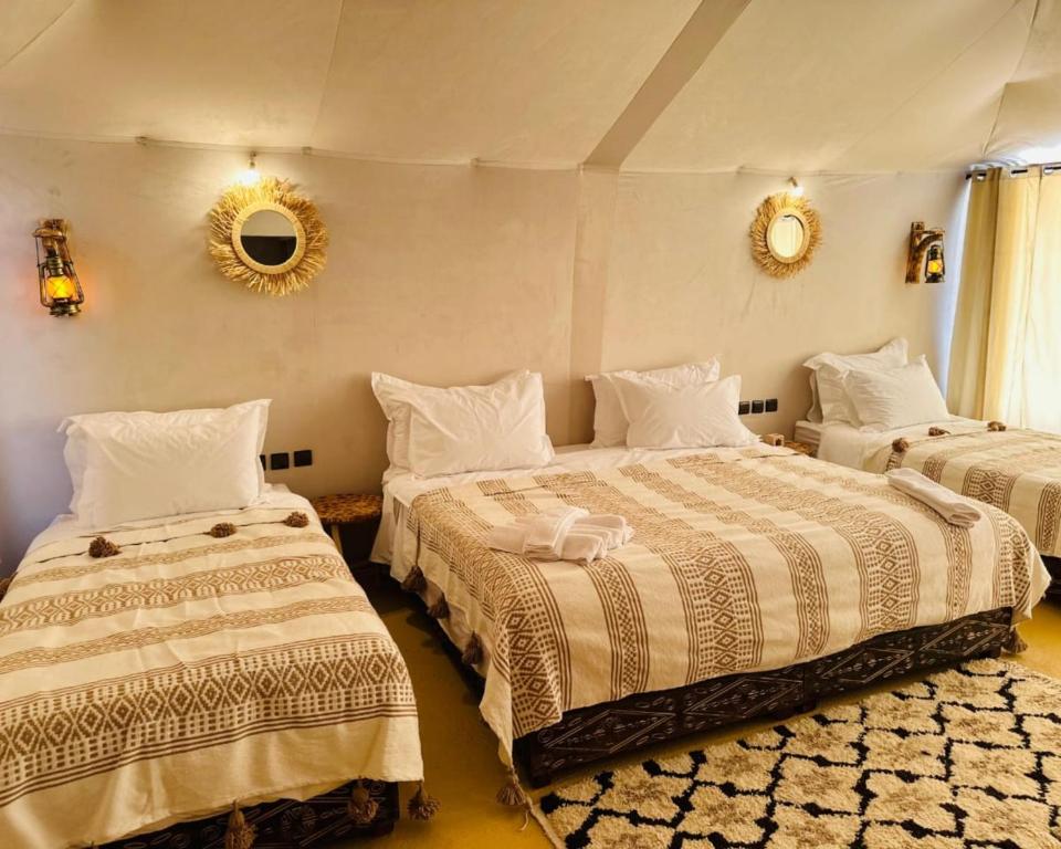 a bedroom with two beds and a mirror on the wall at Luxury Desert Central Camp in Merzouga