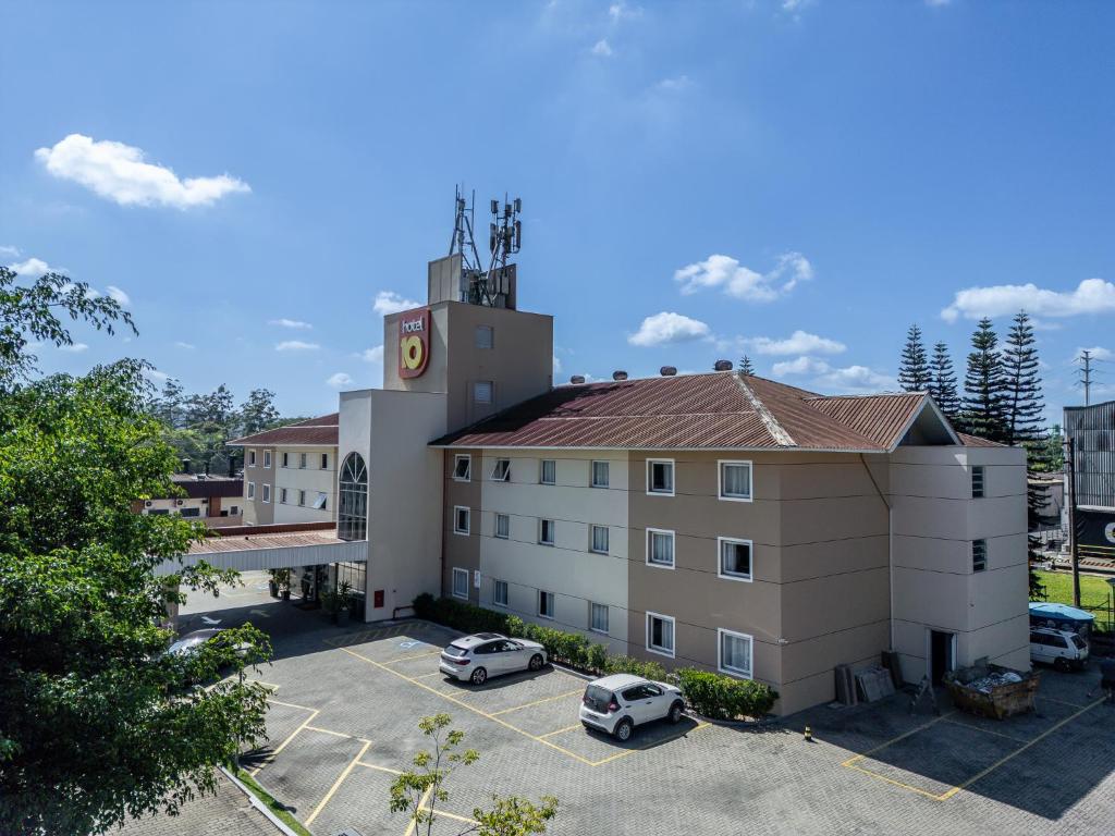ein Hotelgebäude mit auf einem Parkplatz abgestellten Autos in der Unterkunft Hotel 10 Joinville in Joinville