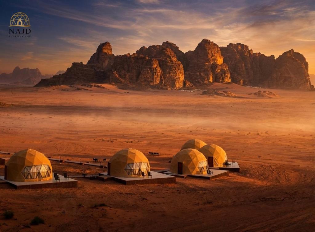 three tents in the desert with mountains in the background at Najd Luxury Camp in Wadi Rum
