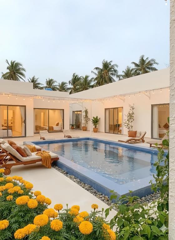 a swimming pool with chairs and flowers in front of a house at Villa Santoni Mũi Né in Mui Ne