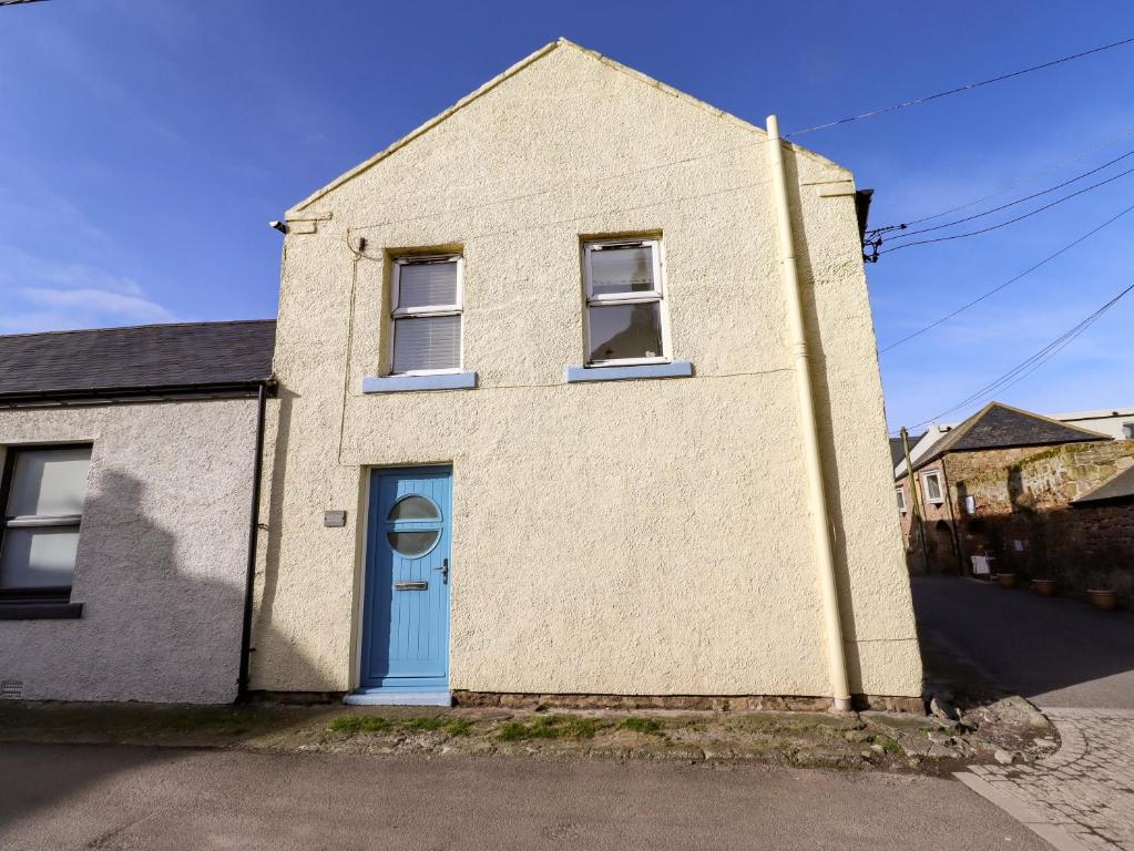 a white brick house with a blue door at Corner Cottage in Seahouses