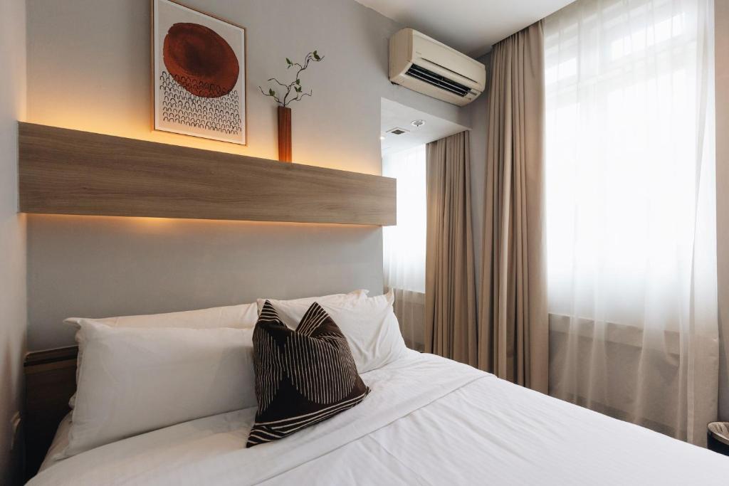 una camera da letto con un letto con cuscini bianchi e una finestra di Hotel NuVe a Singapore