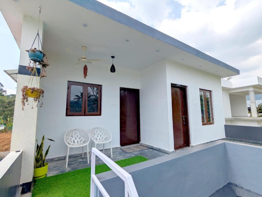 a white house with a balcony with two chairs at Blooms home stay in Thekkady