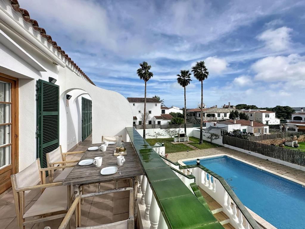 a balcony with a wooden table and a swimming pool at Apartamento con piscina SS19 in Fornells
