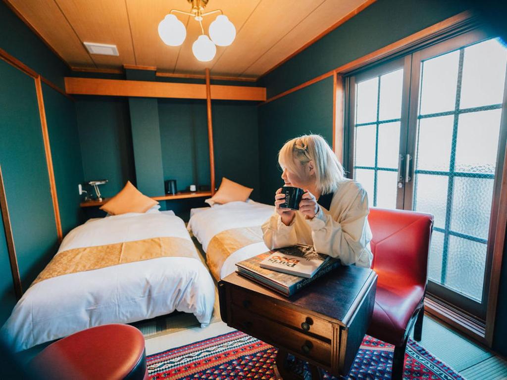 a woman sitting at a desk in a room with a bed at KANSEI null 佐賀 in Saga