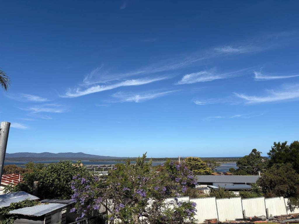 a blue sky with a white fence and trees at Serenity House in Mallacoota