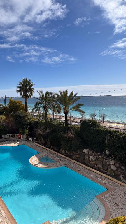 a swimming pool with palm trees and the beach at Séjour bord de mer Résidence avec piscine Cannes in Cannes