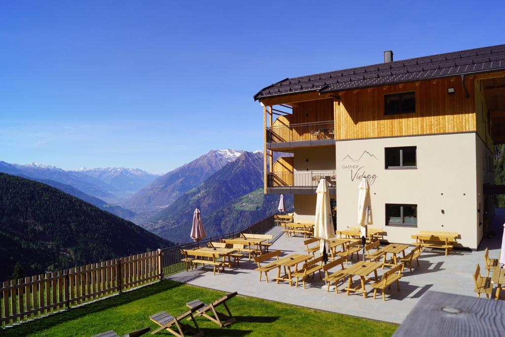 a building with tables and chairs and mountains at Gasthof Videgg in Schenna