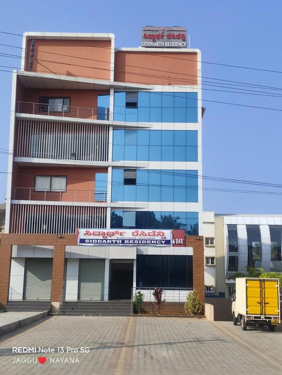 a tall building with a yellow truck in front of it at Siddarth Residency in Channarāyapatna