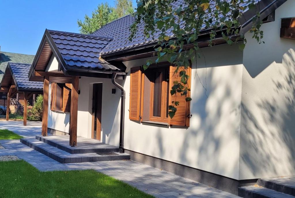 a white house with wooden windows and green grass at Dworek Brzozowy, Augustów Płaska in Płaska