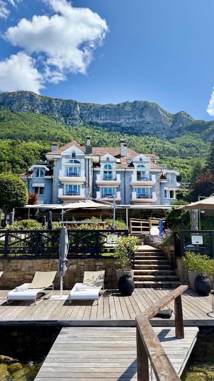 a large house with a deck with chairs and mountains at Hôtel La Maison Bleue par Yoann CONTE in Veyrier-du-Lac