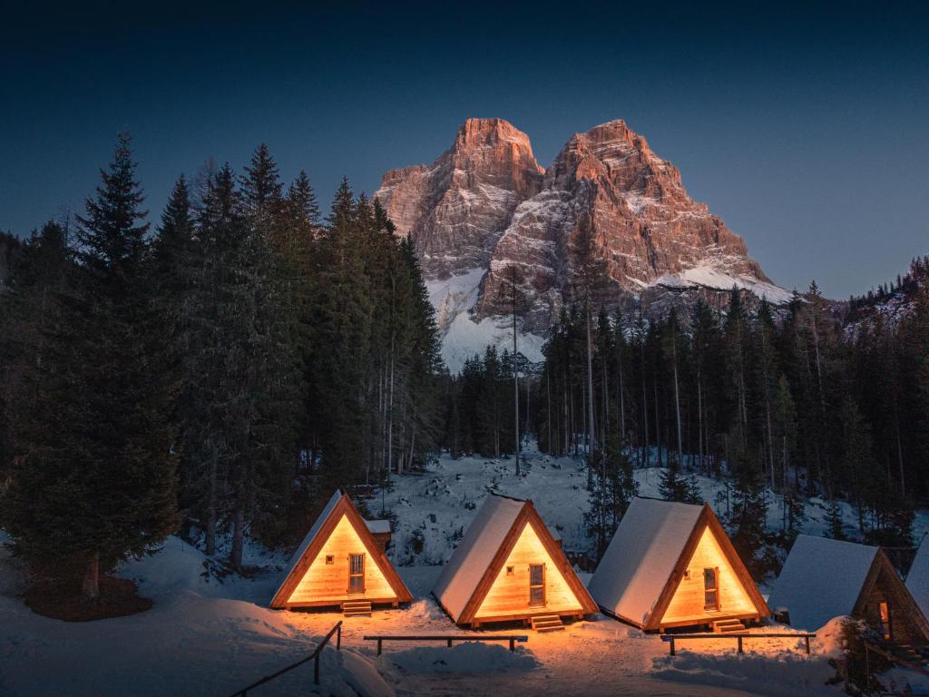 a group of cottages in the snow in front of a mountain at Camping Cadore in Selva di Cadore