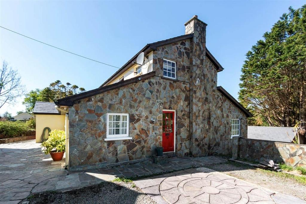 a stone house with a red door on a driveway at Bay View Ridge Cottage in Bantry