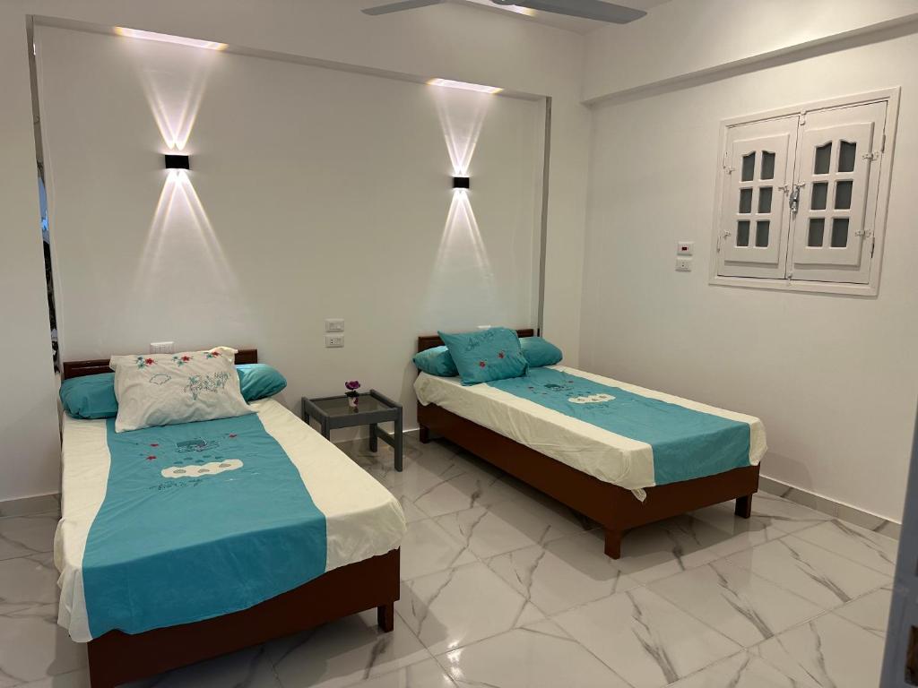 two beds in a white room with blue sheets at golden house in Al Aqālitah