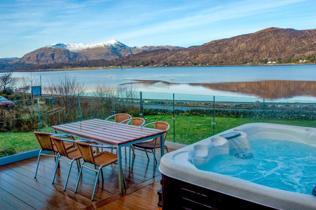a deck with a table and chairs and a bath tub at Glenachulish Bay with Hot Tub in Glencoe