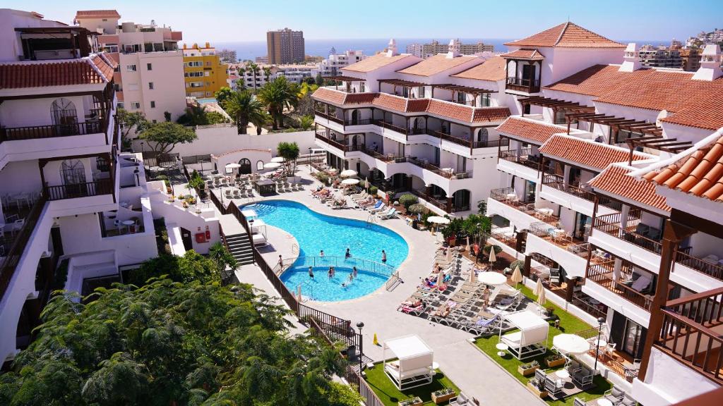 Outdoor pool with sun loungers and umbrellas in a white Mediterranean complex with red-tiled roofs and distant sea view at Coral Los Alisios in Los Cristianos