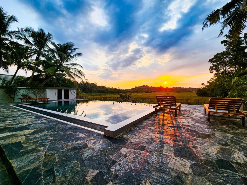 a pool with two benches and a sunset in the background at Ever Breeze Villa Ahangama in Ahangama
