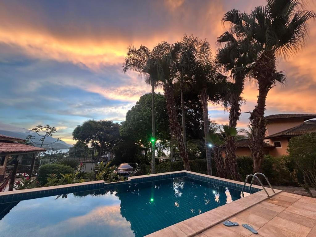 a swimming pool with palm trees and a cloudy sky at Micas House in Ilhabela