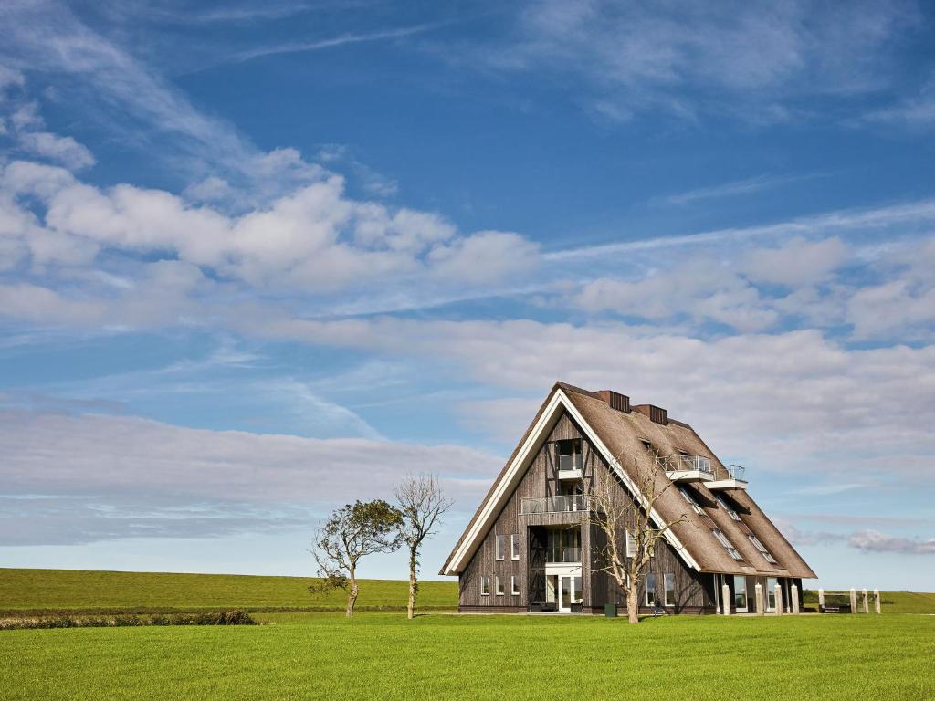 a large wooden barn in a field with trees at Modern large villa on the mudflats in Friesland in Wierum