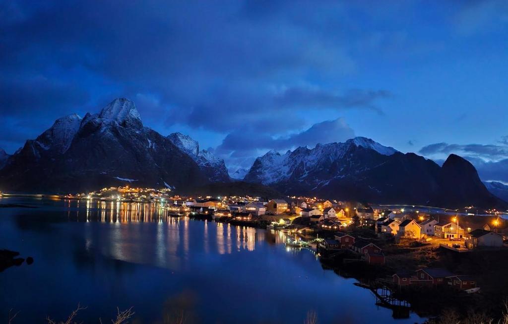 a town on the water in front of mountains at night at Apartment at Lofoten. Mølnarodden. in Sund