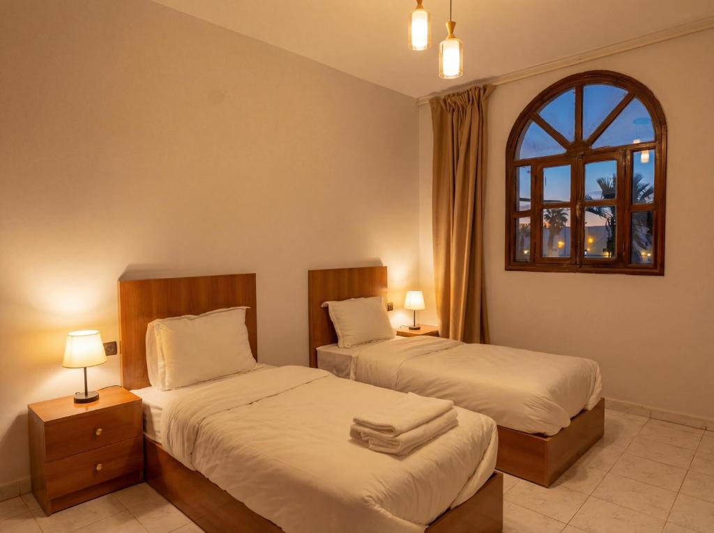 two beds in a room with two lamps and a window at Erraha Hostel Dakhla in Dakhla