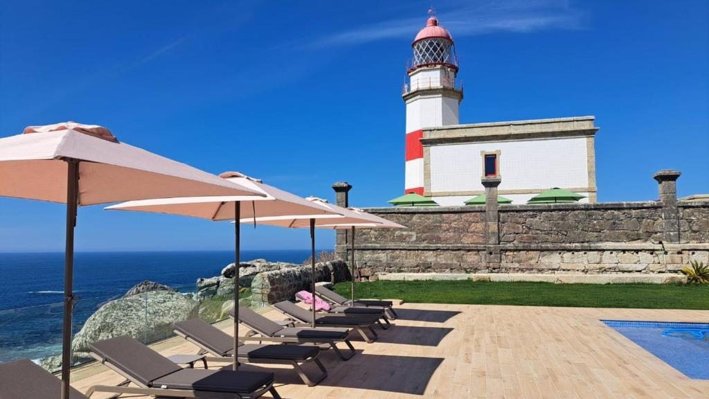 a lighthouse with a row of chairs and an umbrella at Hotel Boutique Faro Silleiro in Baiona