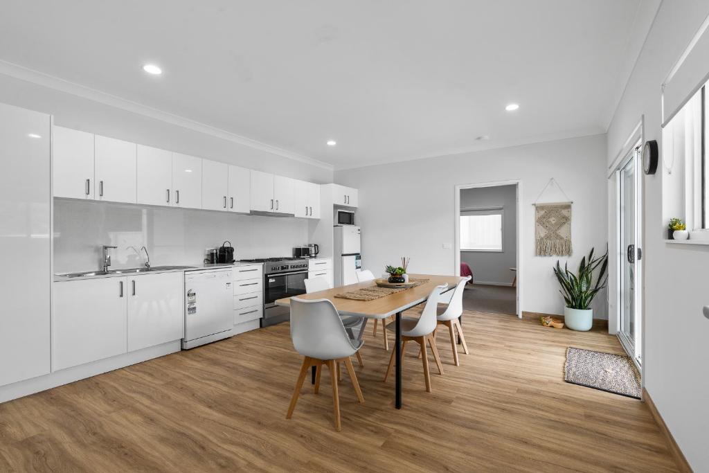 a kitchen with white cabinets and a wooden table and chairs at Misons Guesthouse in Mollymook