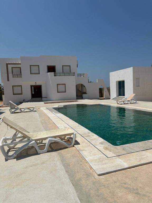 a swimming pool with two lounge chairs next to a building at Les jardins de Sara in Mellita