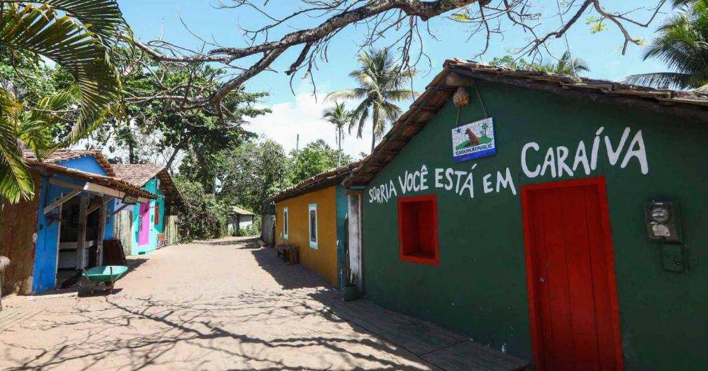 a green building with a red door on a street at Pousada Cristal - Caraiva in Porto Seguro