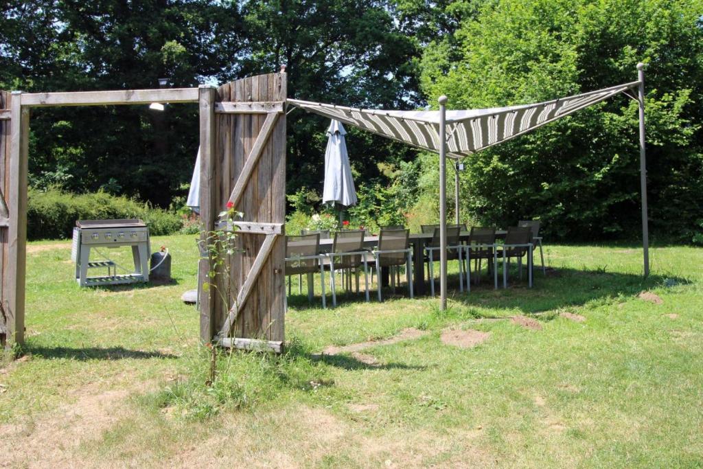 a wooden arch with chairs and a table with an umbrella at Petite gare aux oiseaux in Le Châtenet