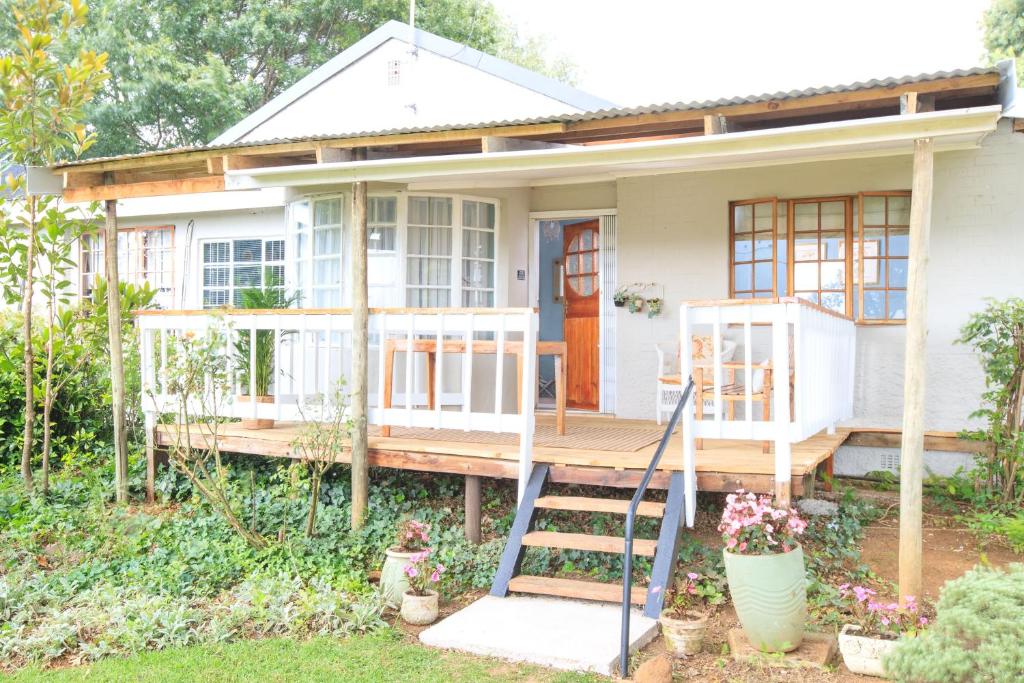 a small white house with a porch and stairs at JoyWood Cottages in Himeville