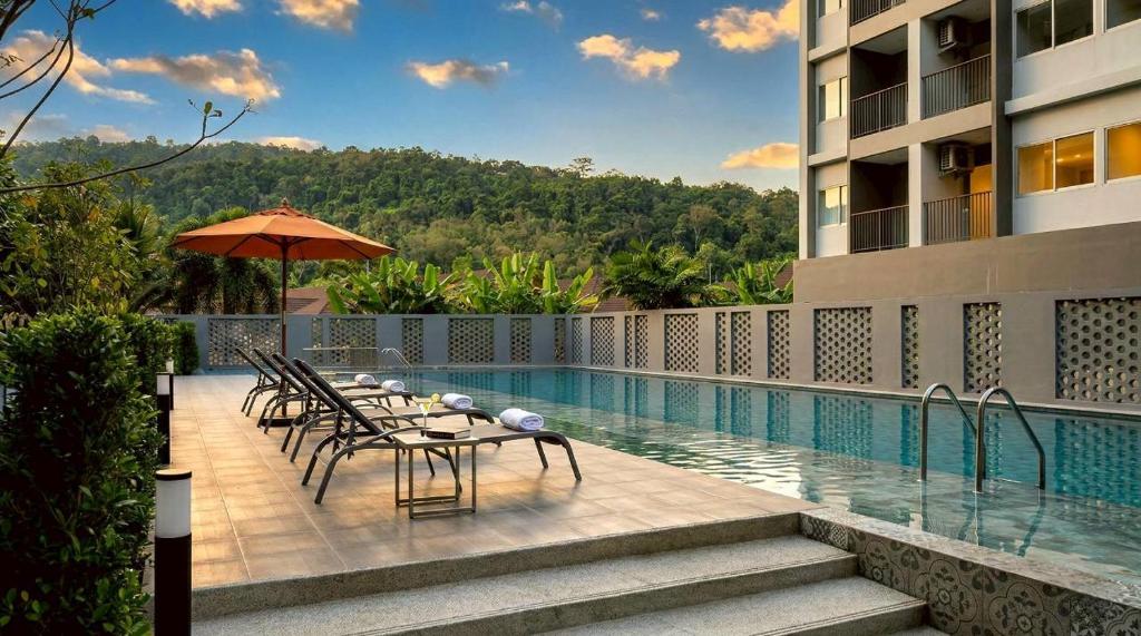 a table with chairs and an umbrella next to a swimming pool at Beehive Boutique Hotel Phuket in Phuket