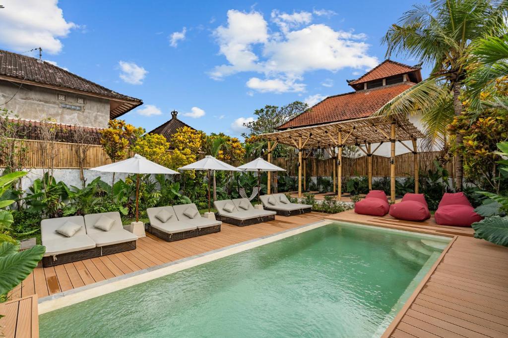 a pool with chairs and umbrellas next to a house at Palermo Suites by DH in Ubud