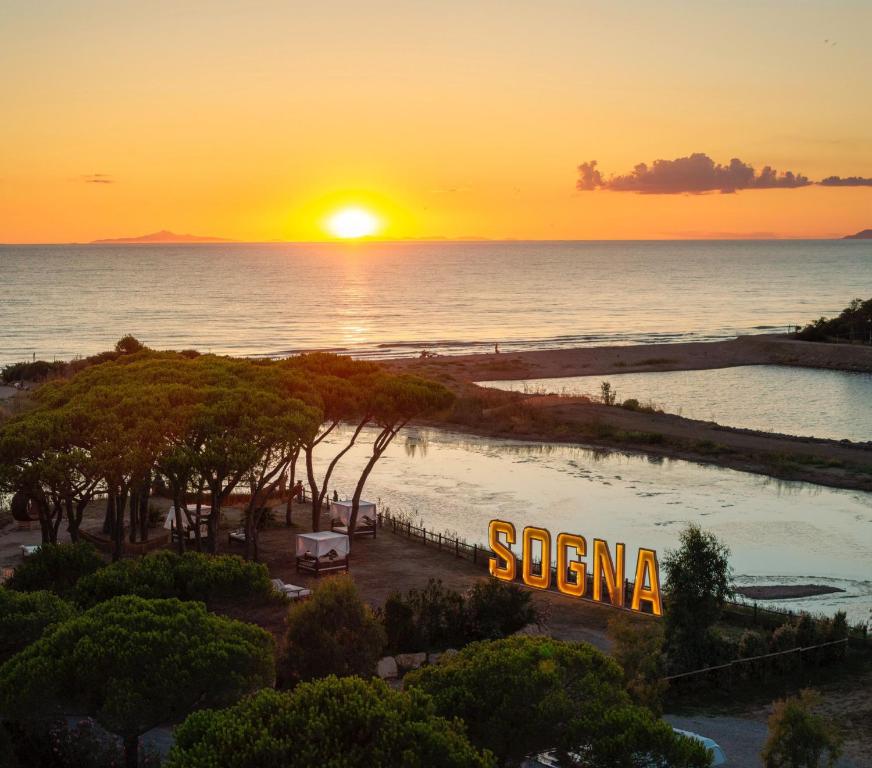 a sunset over a beach with a sign that reads sonanza at NOMAD ARGENTARIO - Area Sosta Camper - NO TENDE - NO CARAVAN - Empty Pitch Only Campervan RV - SOLO PIAZZOLA PER IL PROPRIO CAMPER - Tariffa fino a 4 persone - TUTTI I SERVIZI INCLUSI in Albinia