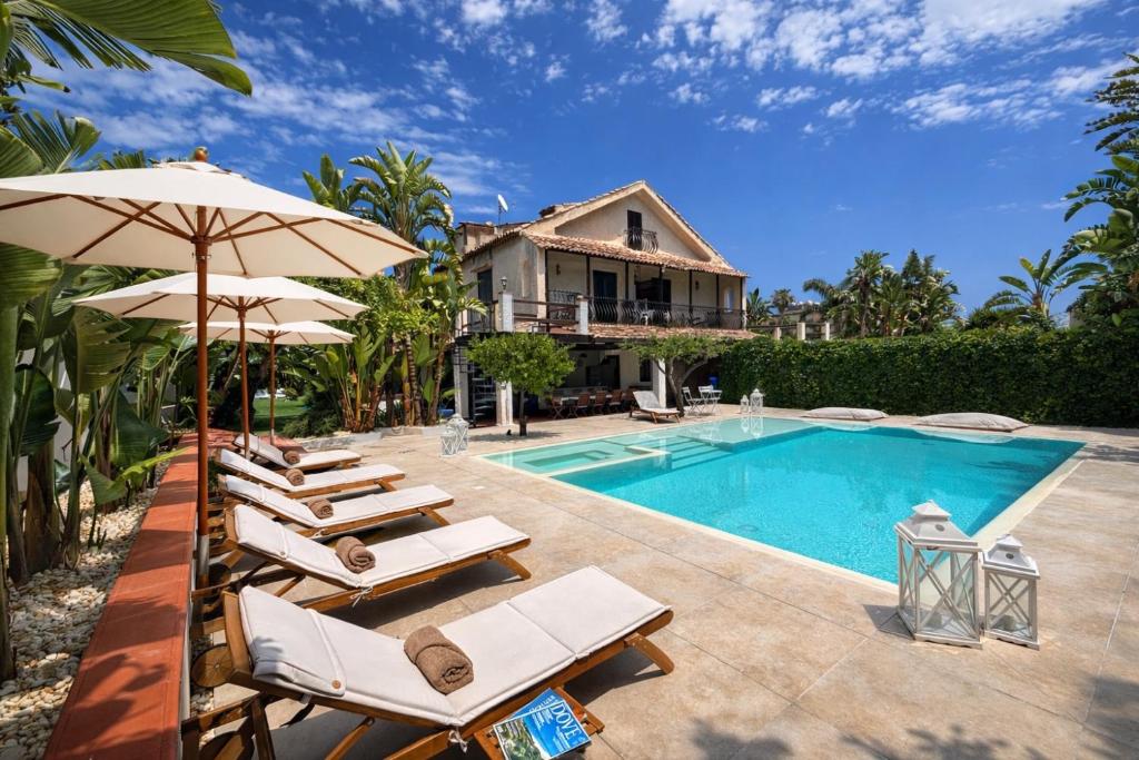 a pool with chairs and umbrellas next to a house at Villa Elisa - Luxury and Style by the Sea in Fontane Bianche