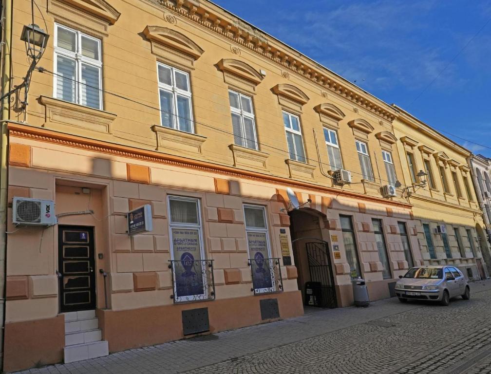 a yellow building with a car parked in front of it at Apartmani u srcu grada in Zrenjanin