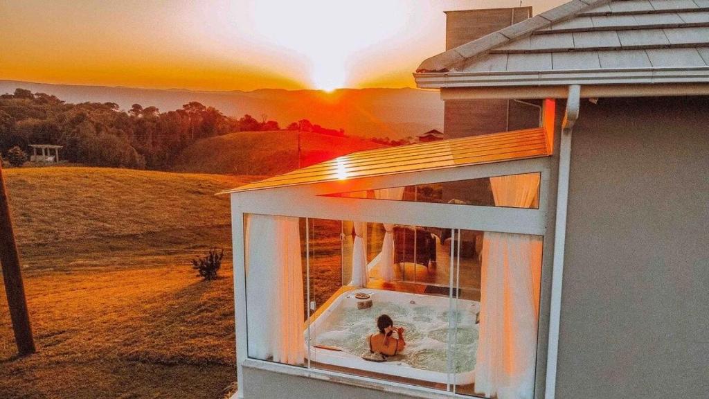 a person sitting in a window with the sunset in the background at Casa Paraíso do Sol - Rancho Queimado - SC in Rancho Queimado
