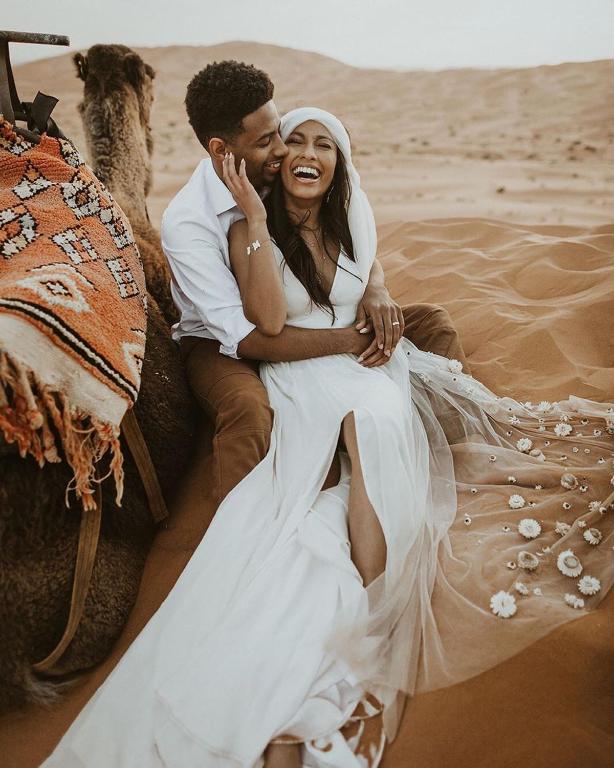 a bride and groom sitting on an elephant in the desert at Khamlia Desert Camp in Merzouga