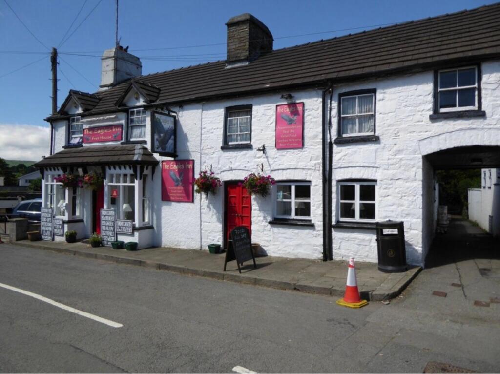 a white building with a red door on a street at Cosy Pubs Bed & Breakfast in Rhayader