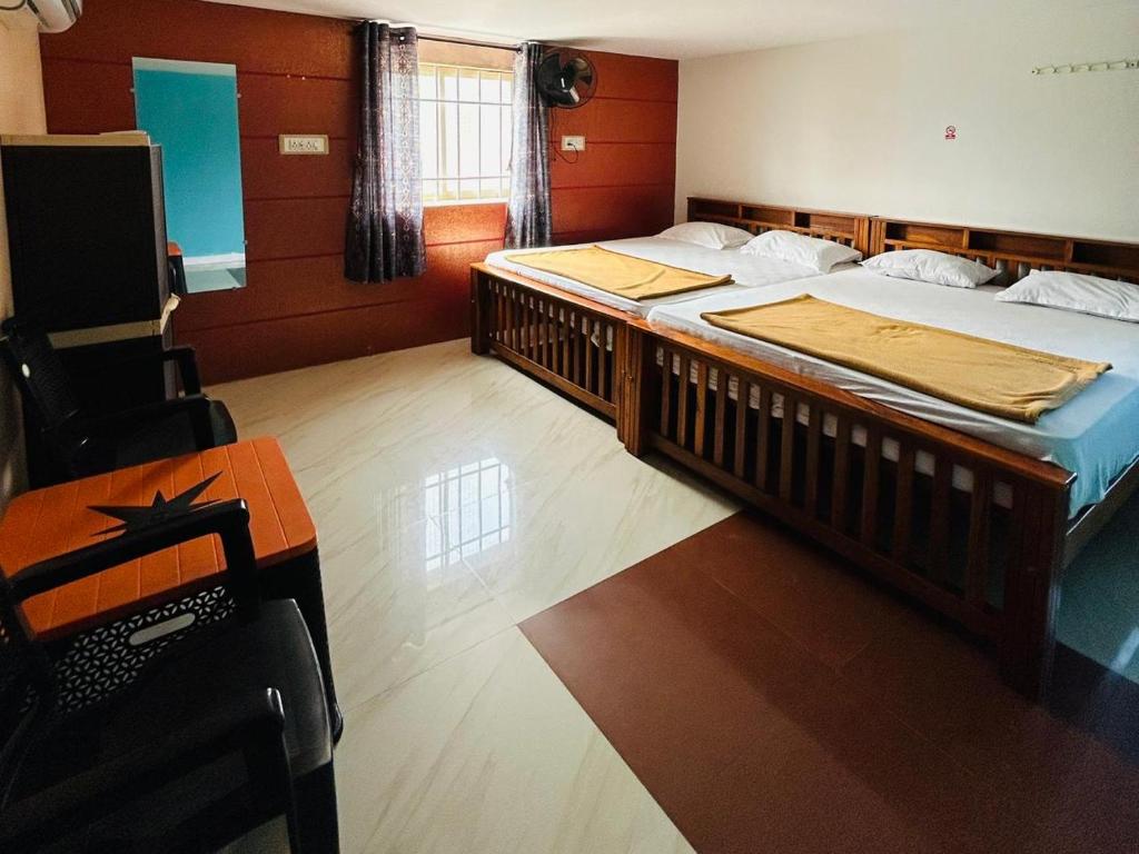 two beds in a room with a table and a desk at Comforts Bhairavi INN in Kalyānpur